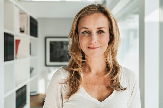 Confident smiling woman with blonde hair at home looking at camera
