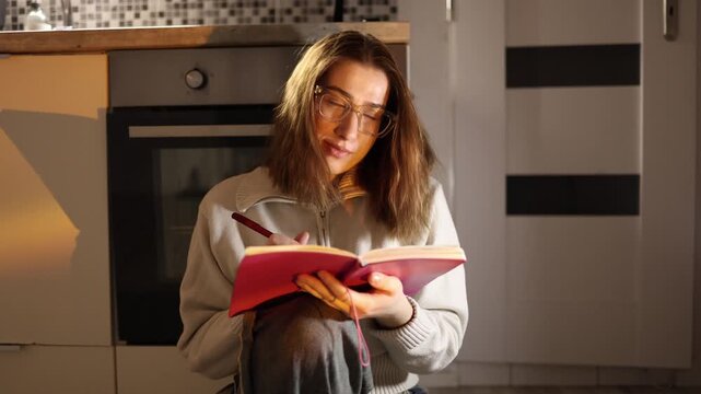 Young woman sitting at home with notebook unable to focus on study constantly distracted by smartphone scrolling instead of learning losing productivity in warm evening atmosphere