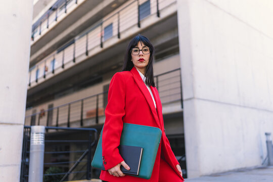 Confident businesswoman in red suit holding portfolio outdoors