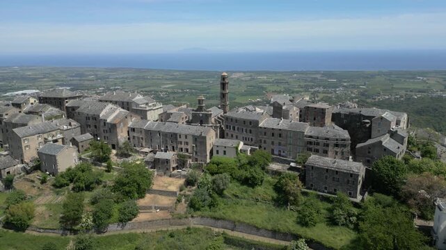 Aerial drone orbit around Penta di Casinca perched village overlooking chestnut valley, Corsica, France