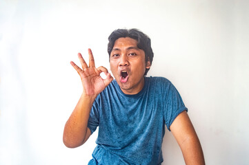 Fototapeta premium A man in a blue shirt is making an OK hand gesture against a plain white background. The image is simple and clear, making it suitable for various uses such as advertisements, blogs, or social media