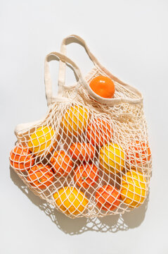 Lemons and tangerines in eco-friendly shopping bag on light gray background, flat lay top view. Mesh cotton string bag filled with citrus fruits. Concept of eco-friendly living, zero waste