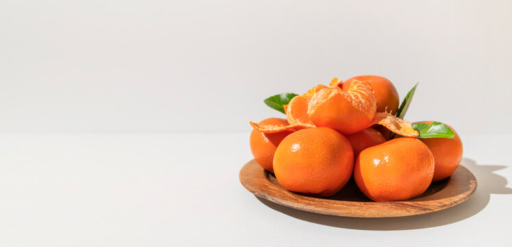 Fresh delicious tangerines with green leaves in wooden plate on light gray background. Orange tangerines, citrus fruit. Summer background with tangerines, top view, space for text
