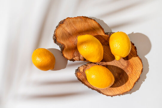 Yellow ripe lemons lie on wooden podium with sunny shadow from tropical leaf on white background. Summer background with lemons, citrus fruit source of vitamin C. Lemon mockup