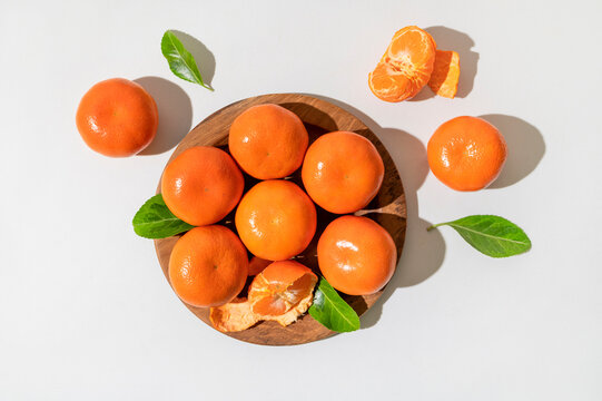 Fresh delicious tangerines with green leaves in wooden plate on light gray background. Orange tangerines, citrus fruit. Summer background with tangerines, top view, space for text