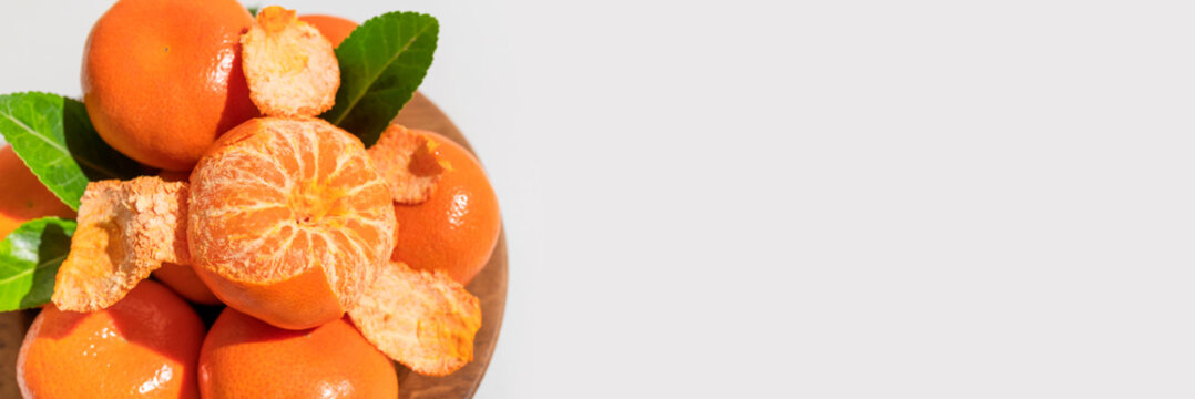 Fresh delicious tangerines with green leaves in wooden plate on light gray background. Orange tangerines, citrus fruit. Summer background with tangerines, top view, space for text
