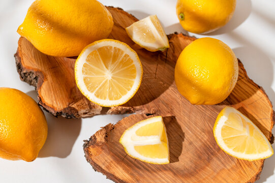 Yellow ripe lemons lie on wooden podium with sunny shadow from tropical leaf on white background. Summer background with lemons, citrus fruit source of vitamin C. Lemon mockup