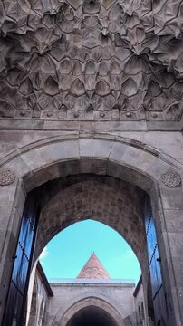 Vertical tilt shot from a massive wooden door archway to a traditional conical stone roof. Captures the depth of the historic courtyard