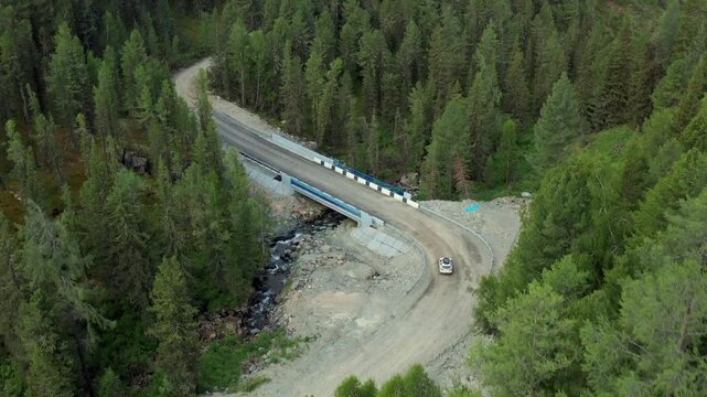 Aerial view of mountain road crossing river bridge in Katon Karagay national park, East Kazakhstan. Scenic Altai forest landscape, remote wilderness travel and natural environment.