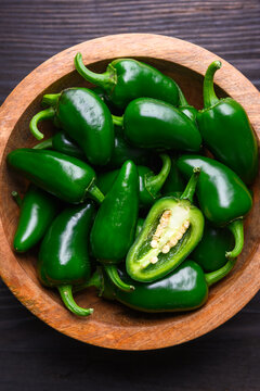 Wooden bowl filled with jalapeno peppers on dark table close view. Fresh green chili composition rustic food background