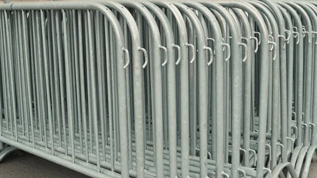 Metal crowd control barriers are lined up neatly in a public area, preparing for an upcoming event. The barriers are arranged in rows, indicating a setup for managing crowds and guiding attendees