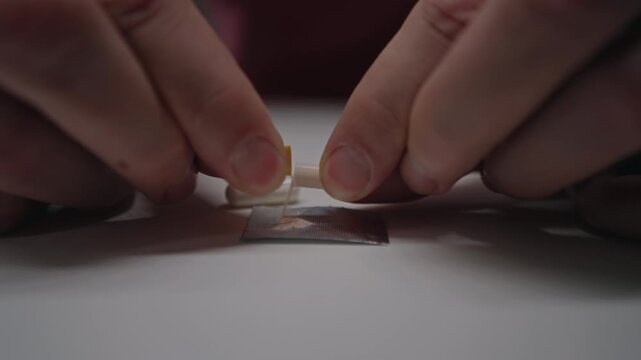 Hands opening and mixing powder contents of several different medication capsules on small piece of foil, creating customized pharmaceutical compound for medical therapy, close-up, slow motion.