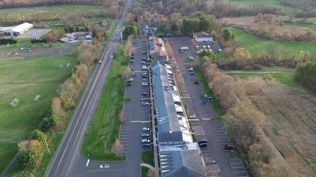 Long commercial building along York Rd in Buckingham Township stands opposite wide recreation fields with scattered soccer goals. Gray roofing, parked vehicles, early season foliage combine, PA