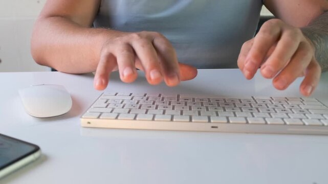 Close view of man typing on compact wireless keyboard with mouse and smartphone on desk. Modern workspace, digital activity, online communication, remote work and everyday computer usage scene.