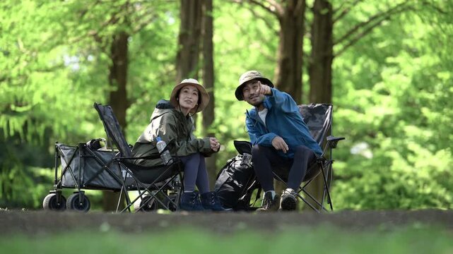 新緑のキャンプ場で椅子に座る笑顔のアウトドアやレジャーを楽しいミドルの夫婦　鳥や景色を眺める動画　指を差して見つめる	