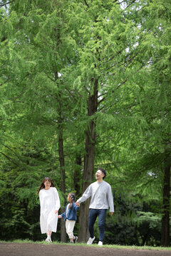 A happy family walking hand in hand in a park with fresh greenery&mdash;full-body vertical shot