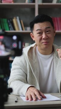 A man smiles and gives a thumbs-up gesture while recording himself with a smartphone on a tripod, preparing for a video presentation