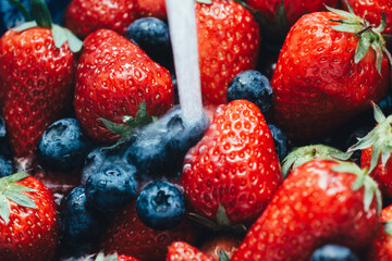 Obraz premium Fresh strawberries and blueberries being rinsed under running water in a close-up shot