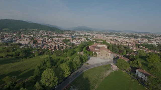 Aerial drone view of the Sant'Agostino monastery and the Fara green field in Bergamo Upper Town, showcasing the Gothic facade and the scenic surrounding landscape