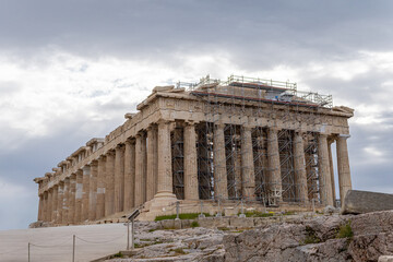 Fototapeta premium Full view of the ancient Parthenon temple in Athens, Greece, showing Doric columns and ongoing restoration work with scaffolding. Iconic world heritage site under a cloudy sky.