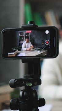 A man is filming himself with a smartphone mounted on a tripod, creating content for his online channel