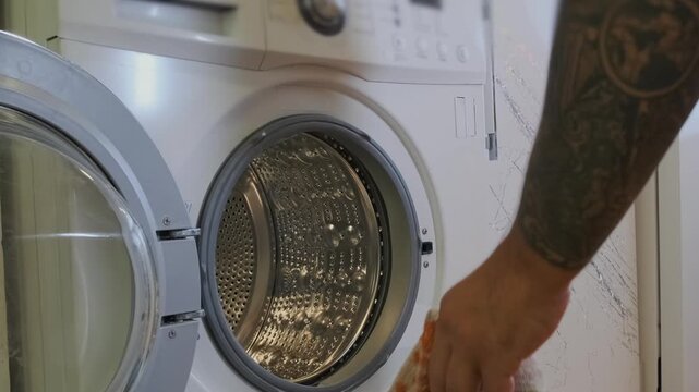Man placing dirty clothes into front load washing machine at home. Household laundry routine, sorting garments before wash, domestic chores, everyday cleaning and home maintenance lifestyle scene.