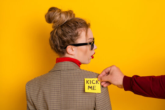 Young Woman in Trendy Glasses with Kick Me Note on Her Jacket on Yellow Background