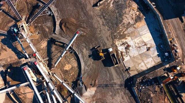 Aerial view of industrial conveyor belts and piles of gravel. Top view of aggregate production facility with conveyor belts transporting crushed stone and industrial machinery.