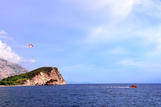 Picturesque view of Adriatic sea, St. Nicholas Island and tourists on a parachute, Budva, Montenegro. Topic of summer vacation, leisure for adventure tourist. Popular tourist pastime with parascending