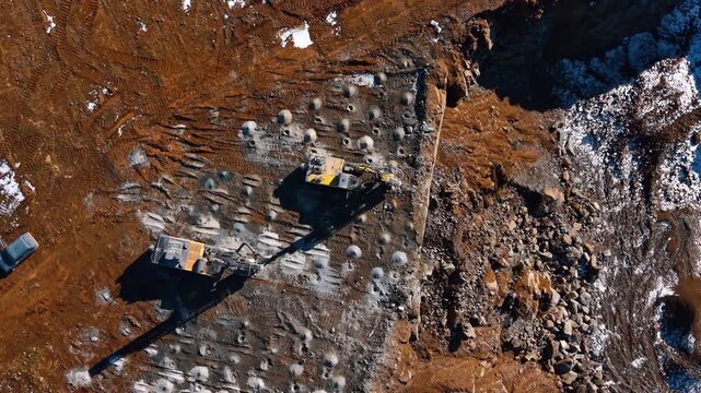 Top down view of drilling rigs creating blast pattern. Symmetrical pattern of drilled holes made by heavy machinery on the ground surface of an open pit mine.