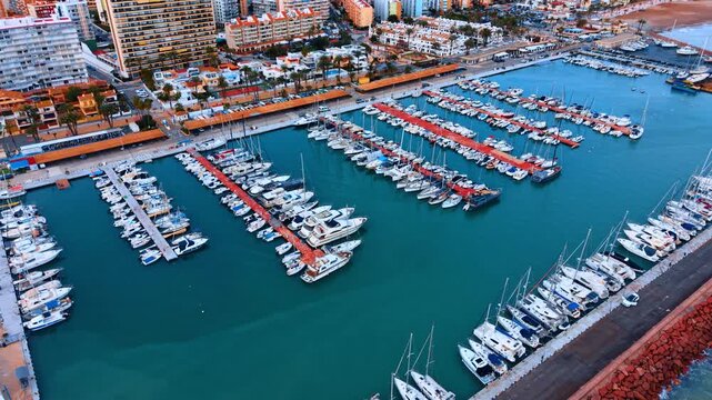 High angle perspective of yachts docked in harbor. Aerial view showing rows of white boats at red piers in turquoise water.