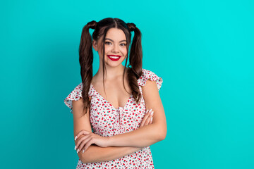 Young glamorous woman with ponytails wearing a floral dress smiles confidently against teal...