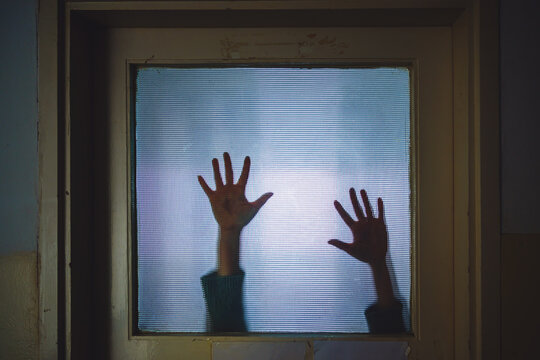 Shadow of woman&rsquo;s hands on frosted glass descending slowly, suspenseful crime concept with trapped victim mood