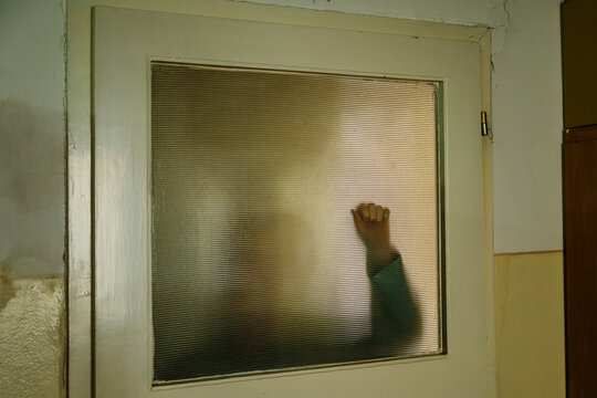 Silhouette of frightened woman knocking on glass door, trapped figure behind frosted surface, fear and escape concept, female figure behind stained glass reaching out, crime and suspense