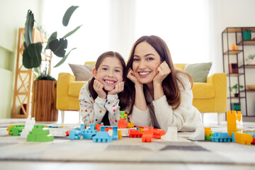 Naklejka premium Mother and daughter lying on the floor playing with colorful building toys and smiling in a bright cozy living room at home