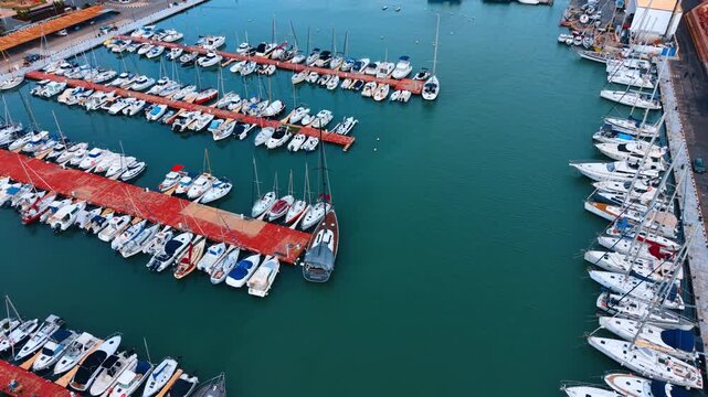 Geometric pattern of yachts docked in turquoise water. High angle aerial shot of numerous white vessels creating a pattern along the red marina piers.