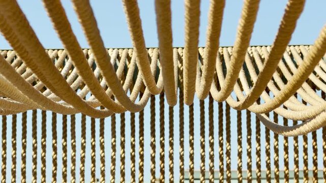 Heavily textured ropes drape gracefully in a rhythmic wave pattern under the sun. This outdoor canopy creates a warm, relaxing shelter that evokes feelings of calm and breezy coastal comfort.