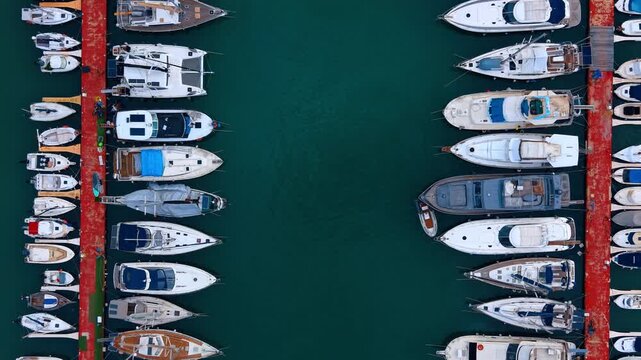 Aerial view of yachts moored at parallel red docks. Yachts and sailing boats docked at red piers in a clear blue harbor.