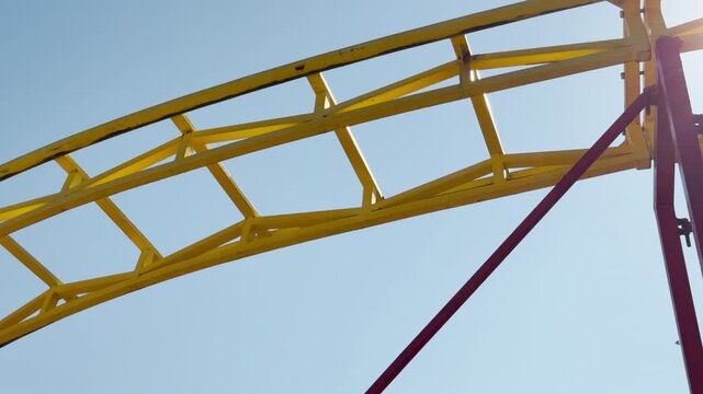 A bright yellow steel roller coaster track curves high in the air against a clear blue sky. It evokes feelings of pure excitement, thrill, and childhood nostalgia for a fun day at the amusement park.