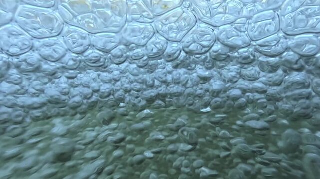 Slow motion bubbles underwater forming in aerated water and drifting toward camera with visible natural light and motion patterns.