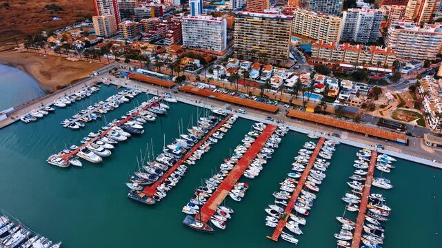 Aerial perspective of marina docks with rows of white boats. Drone shot of multiple red piers with rows of white motorboats and yachts in a Mediterranean marina.