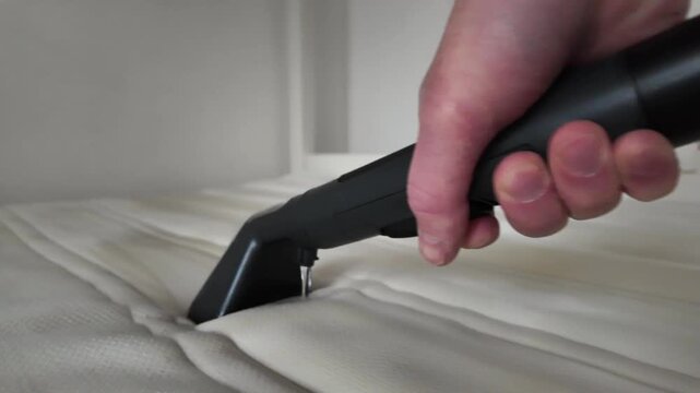 Close-up of a hand deep cleaning a mattress with a vacuum cleaner. Professional housekeeping service for home hygiene, removing dust mites and allergens for better health.
