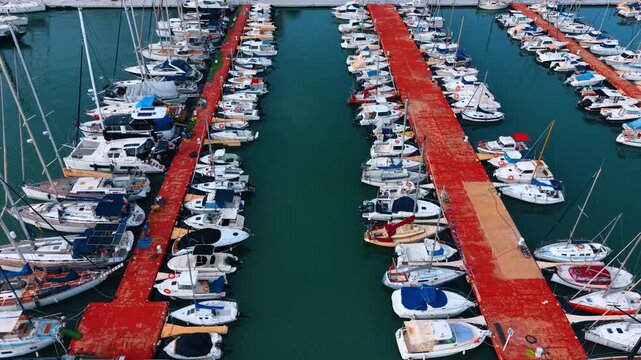 High angle view of motorboats moored at red marina piers. Numerous small and medium motorboats docked at parallel red piers in the turquoise harbor.