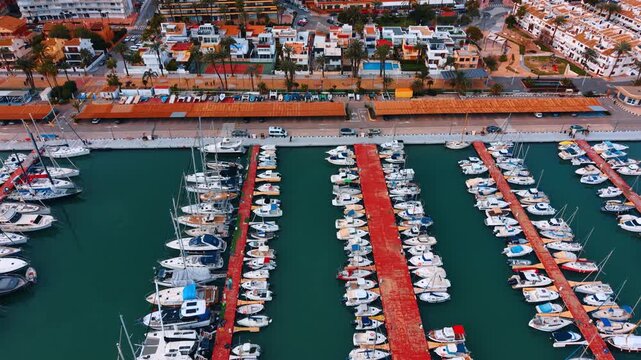 Wide aerial view of marina with coastal city buildings. Panoramic view of a yacht harbor with rows of boats and coastal apartments in the background.