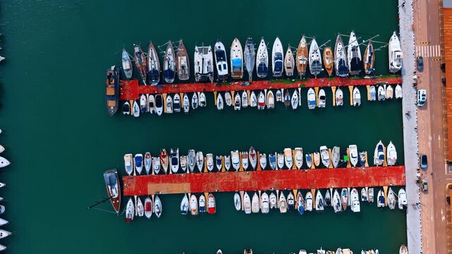Close up top down view of sailing yachts at pier. Detailed aerial view of sailboats and motor yachts moored along a red marina pier.
