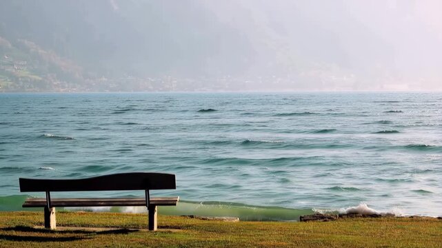 Empty bench facing wavy lake under misty mountain peaks