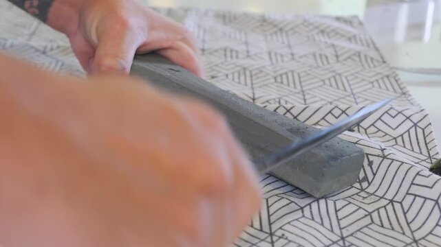 Side view of man sharpening kitchen knife on whetstone, honing blade edge with steady motion. Tool maintenance, kitchen preparation, sharpening process, household skill and safety concept.