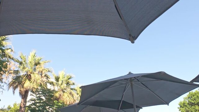Sunbath concept. Under the umbrella by the pool at the hotel. Blue sky and beach umbrella 4k video. Summer vacation, resort hotel.