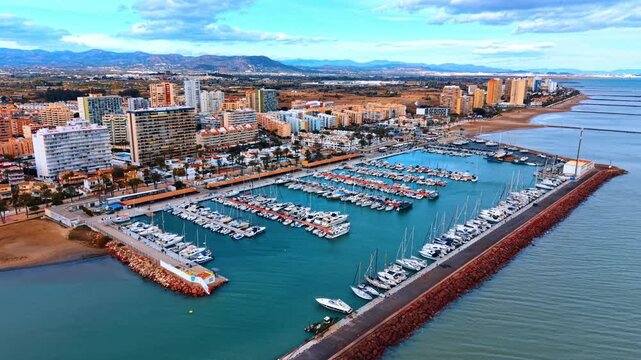 Drone shot of white yachts in turquoise harbor water. High angle perspective of a large marina with rows of boats and coastal infrastructure.