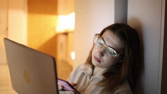 Woman addicted to digital content using laptop and smartphone simultaneously at home evening social media scrolling multitasking distraction overconsumption screen time